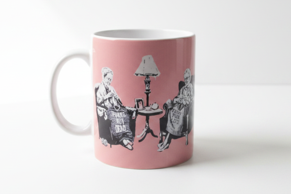 Banksy Punk Grannies pink ceramic mug on clean white surface, bright lifestyle product photography