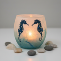 Strawsilk frosted glass seahorse votive tealight holder in aqua blue glowing warmly with lit candle inside