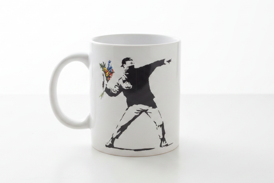 Banksy Love Is In The Air flower thrower ceramic mug on clean white surface, bright lifestyle product photography