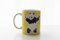 Banksy Panda With Guns yellow ceramic mug on clean white surface, bright lifestyle product photography